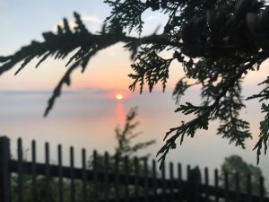 The sun rises on Mackinac Island, as seen from Robinson’s Folly and framed by a fence and a tree branch.