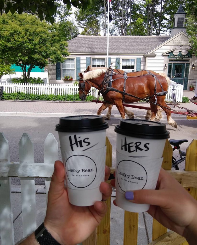 Couple Toasting with Cups of Coffee from Lucky Bean Coffee Shop in Front of Horse-Drawn Carriage on Mackinac Island