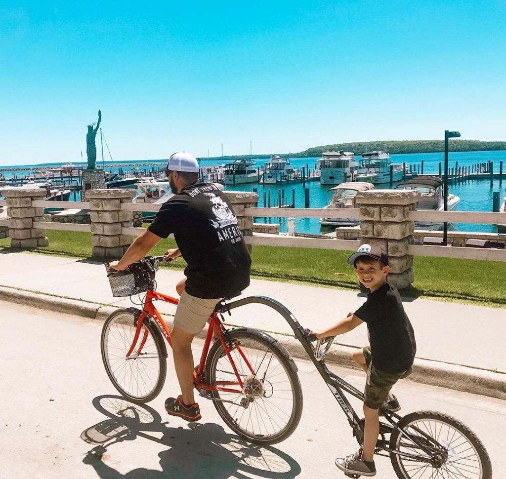 A father and son pedal a tandem bicycle past the marina on Mackinac Island