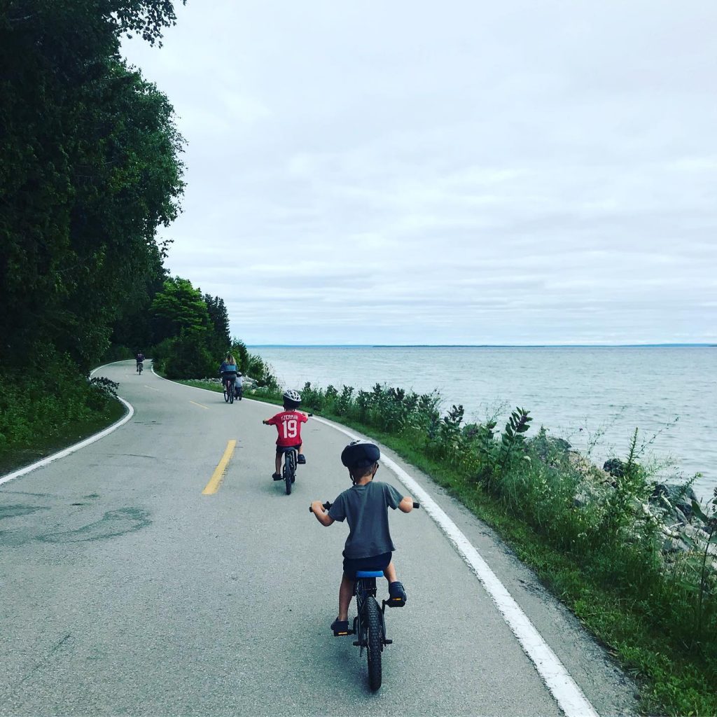 Two Young Boys Riding on Bikes on Highway Overlooking Waters Surrounding Mackinac Island