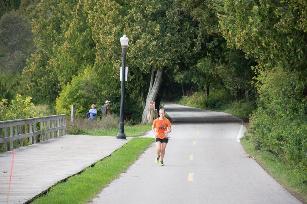 A girl runs on the road near the Mackinac Island boardwalk with trees in the background