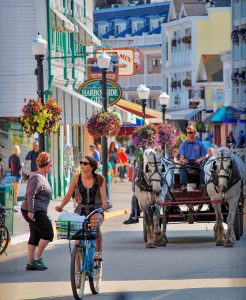 A woman pedals a bicycle down Mackinac Island's Main Street in front of a horse-drawn carriage