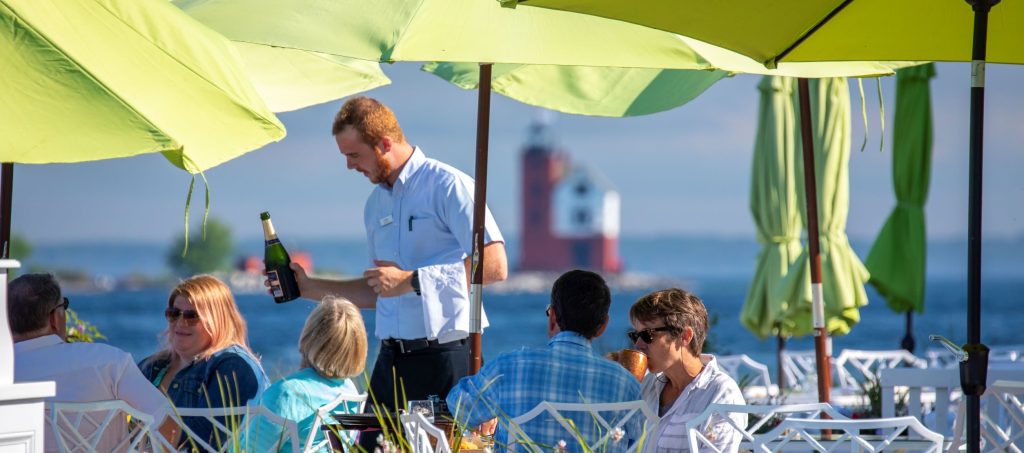 A waiter pours wine into the glasses of diners enjoying a beautiful sunny day on a Mackinac Island waterfront patio
