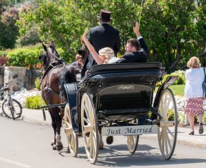 A bride and groom wave to onlookers while enjoying a horse-drawn carriage ride on Mackinac Island