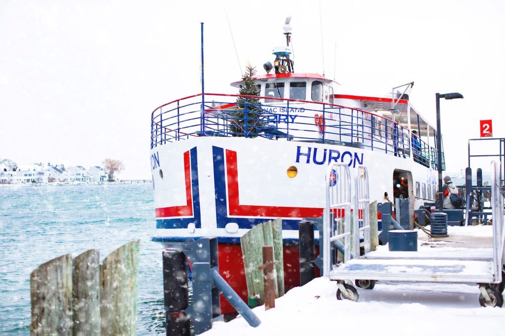 A Mackinac Island ferry boat with a Christmas tree in the bow pulls into the dock on a snowy winter day
